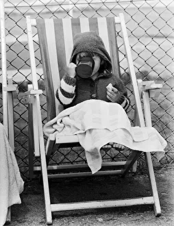 East Sussex Prints: Young child swigs from a mug of juice, whilst sitting on a deck chair