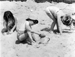 Young children playing in the sand, building sandcastles with a bucket