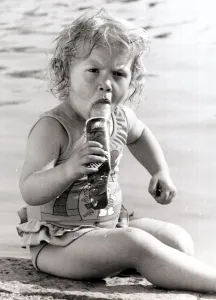 A young girl sits by a swimming pool, cooling off in the heat with a Ice Lolly. 1990