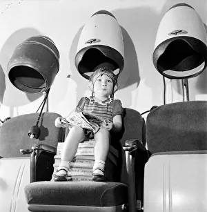 Hairdressers Prints: Young girl sitting with her head under a dryer at her local hairdressers August