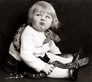 Reptiles Prints: Young girl with a snake wrapped around her pulling a funny face Circa 1960
