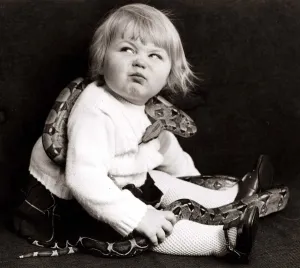 Reptiles Prints: Young girl with a snake wrapped around her pulling a funny face Circa 1960