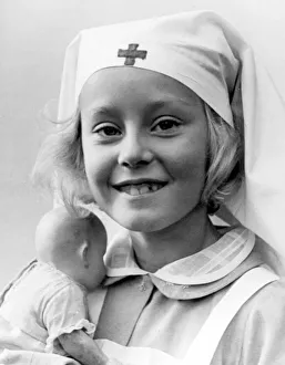 Doll Prints: Young girl wearing a nurse costume holding her toy doll Circa 1945 P044505