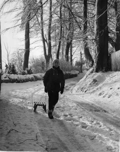 A young lad setting out with his toboggan in a country lane at St Nicholas