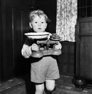 00026 Prints: Young toddler boy holding pair of weighing scales December 1952 C6391-001
