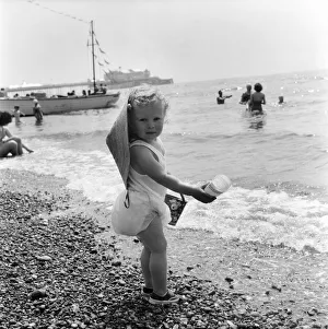 Coast Prints: Young toddler on Brighton Beach goes for a paddle in the sea during the hot summer